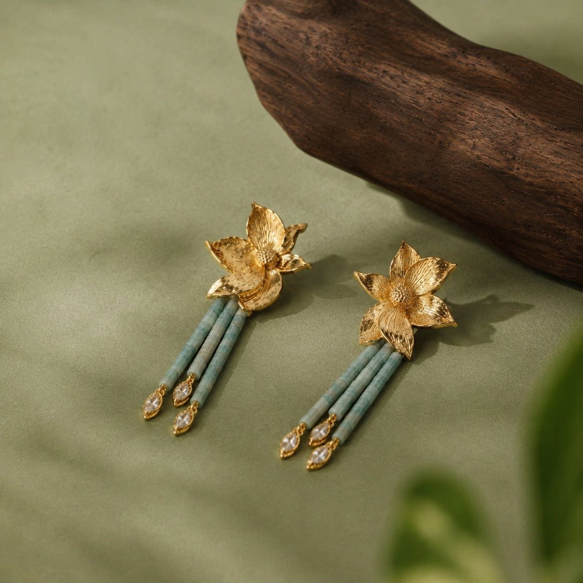Pair of long floral earrings arranged diagonally on a muted green background