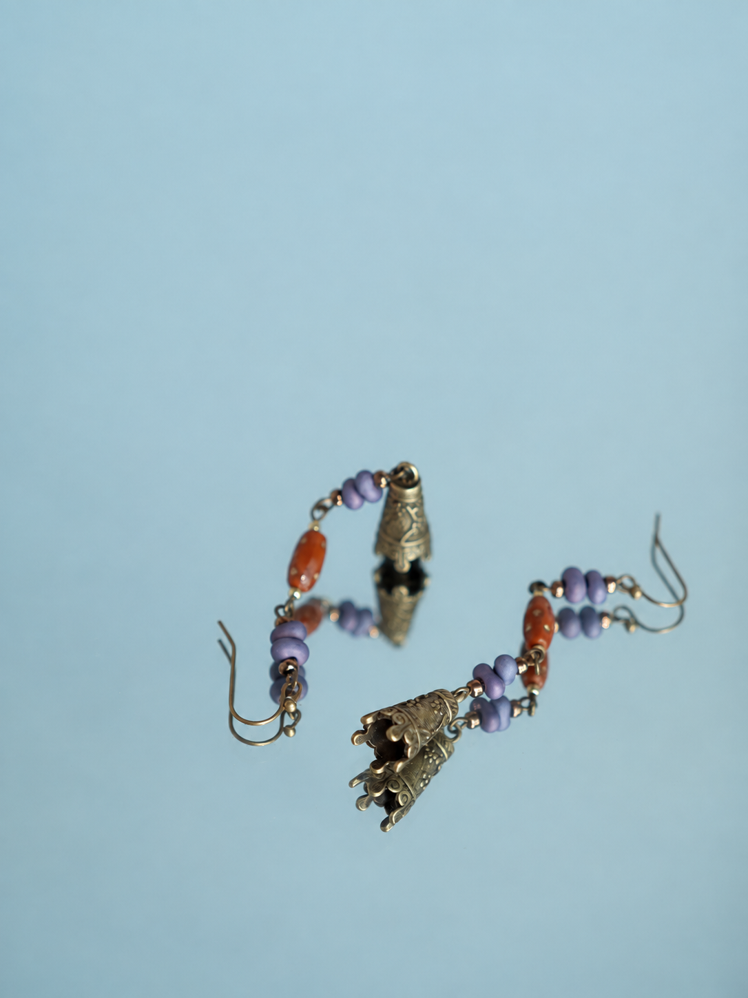 Hua Ling bell earrings with purple beads and patterned charms reflected on a mirror, angle view
