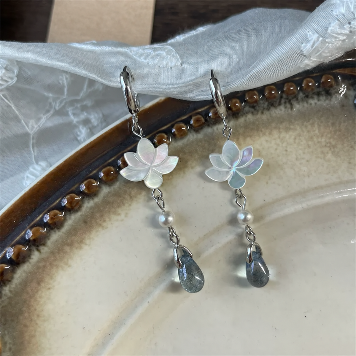 White mother-of-pearl lotus earrings with glass teardrops on a ceramic plate