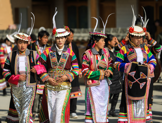 Four people wearing colorful garments and white feathered hats