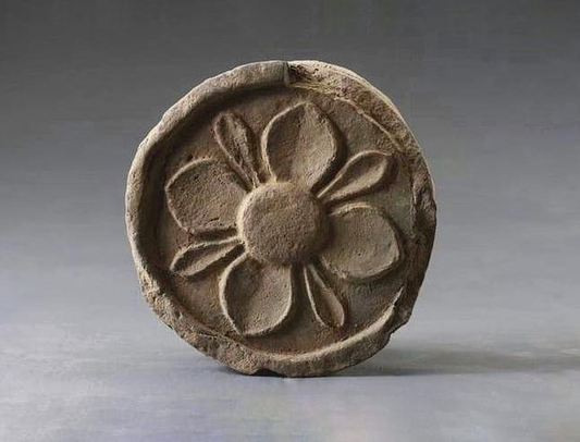 Round relief object with four broad petal-like lobes and smaller pointed elements