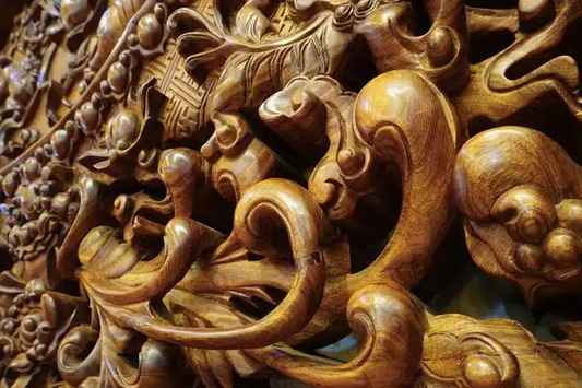 Close-up of a polished wooden relief with layered botanical forms and flowing scrollwork