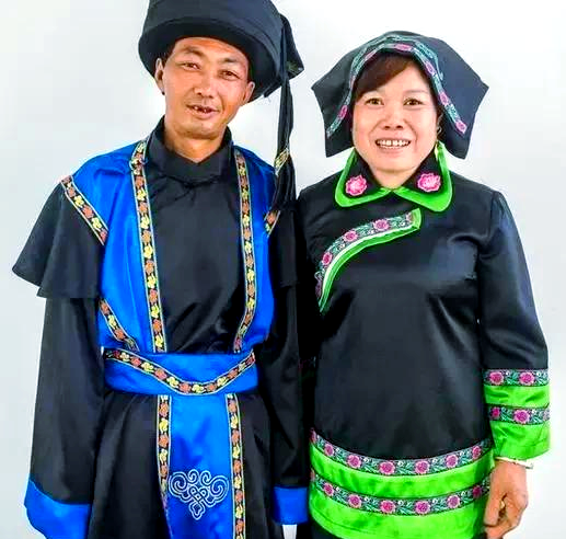 Two adults wearing dark garments with blue and green panels, floral trim and wrapped headwear