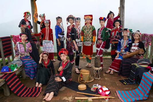 A group presentation of De’ang traditional clothing, musical instruments, and woven objects in a mountain setting.