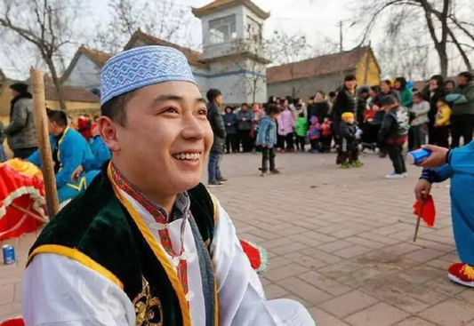 A participant wearing an embroidered cap and vest at an outdoor community celebration