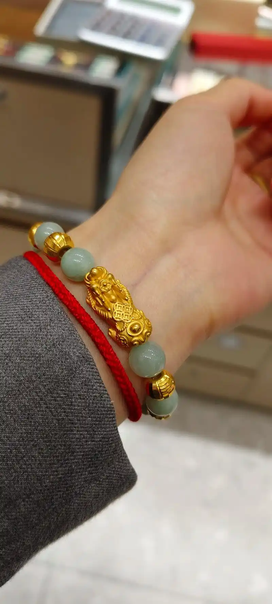 A gold-tone Pixiu bracelet with pale green beads worn on the wrist