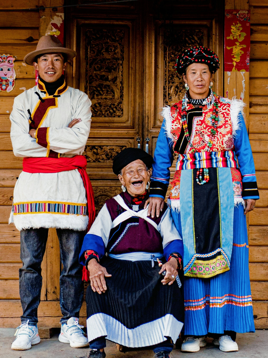 Pumi family wearing traditional clothing in front of a wooden house