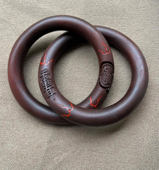 Two dark wooden circular rings inspired by the Qiankun Circle, photographed on a neutral fabric background.