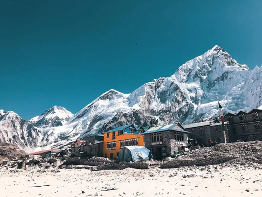 Stone buildings and a colorful lodge beneath snow-covered Himalayan mountains