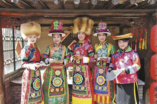 Five women wearing varied embroidered festival costumes and ceremonial hats at a cultural presentation