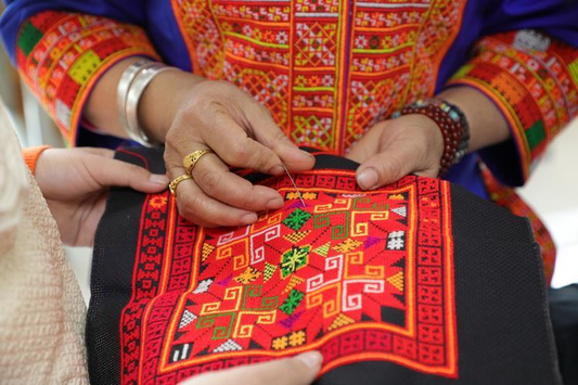 Hands stitching a red, green and yellow geometric textile panel on dark cloth