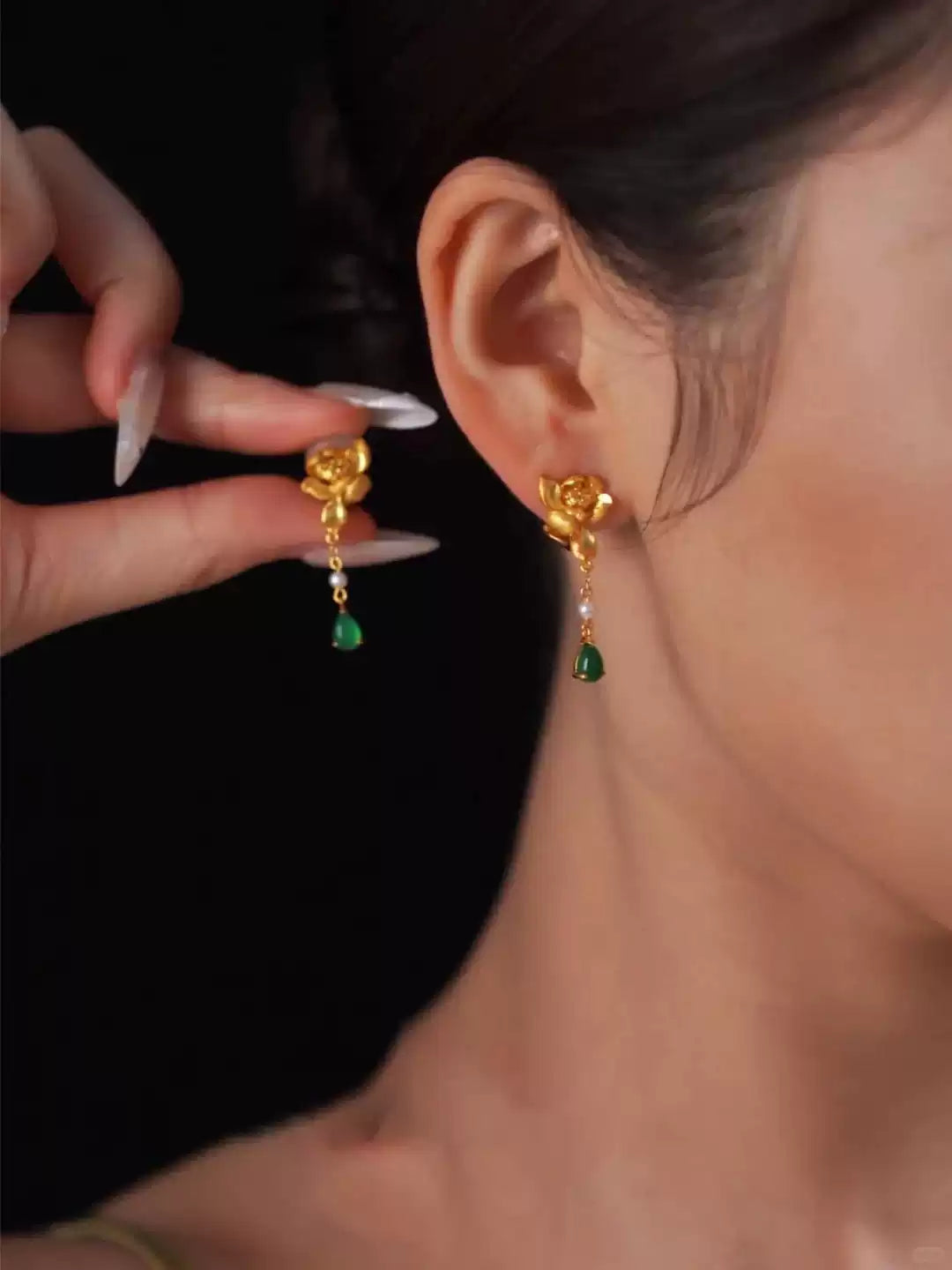 Gold-tone lotus-style drop earrings with green teardrop accents, shown worn