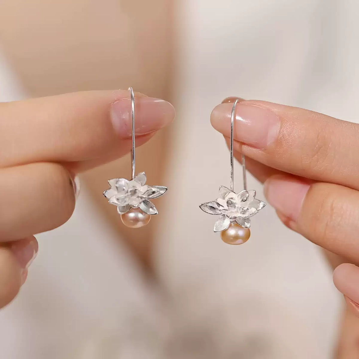 Lotus pearl drop earrings held for scale