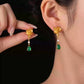 Side view of a gold-tone lotus-style drop earring with green accent