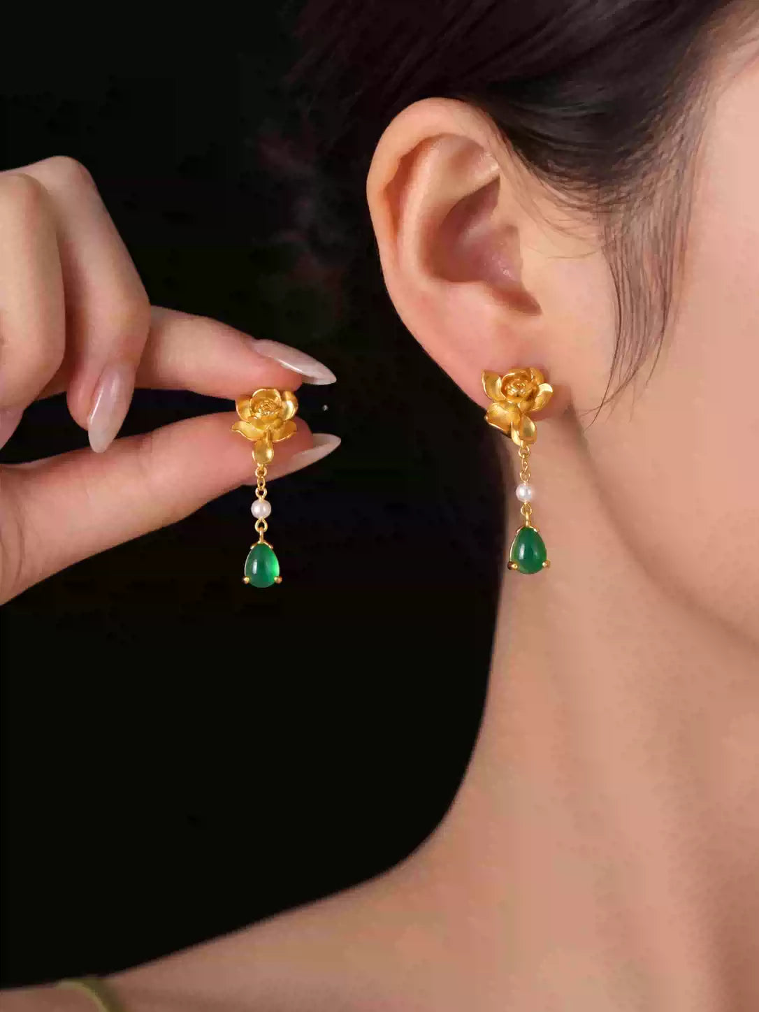Side view of a gold-tone lotus-style drop earring with green accent