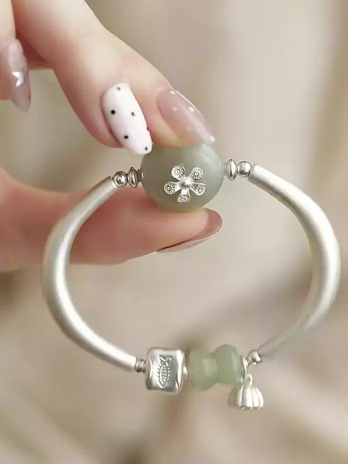 Front detail of the open cuff bracelet with fish-pattern accent and lotus pod pendant