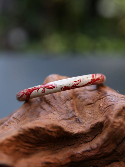 Angled close-up of a pale bangle with red koi and iridescent inlay
