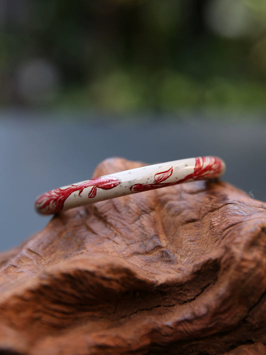 Angled close-up of a pale bangle with red koi and iridescent inlay