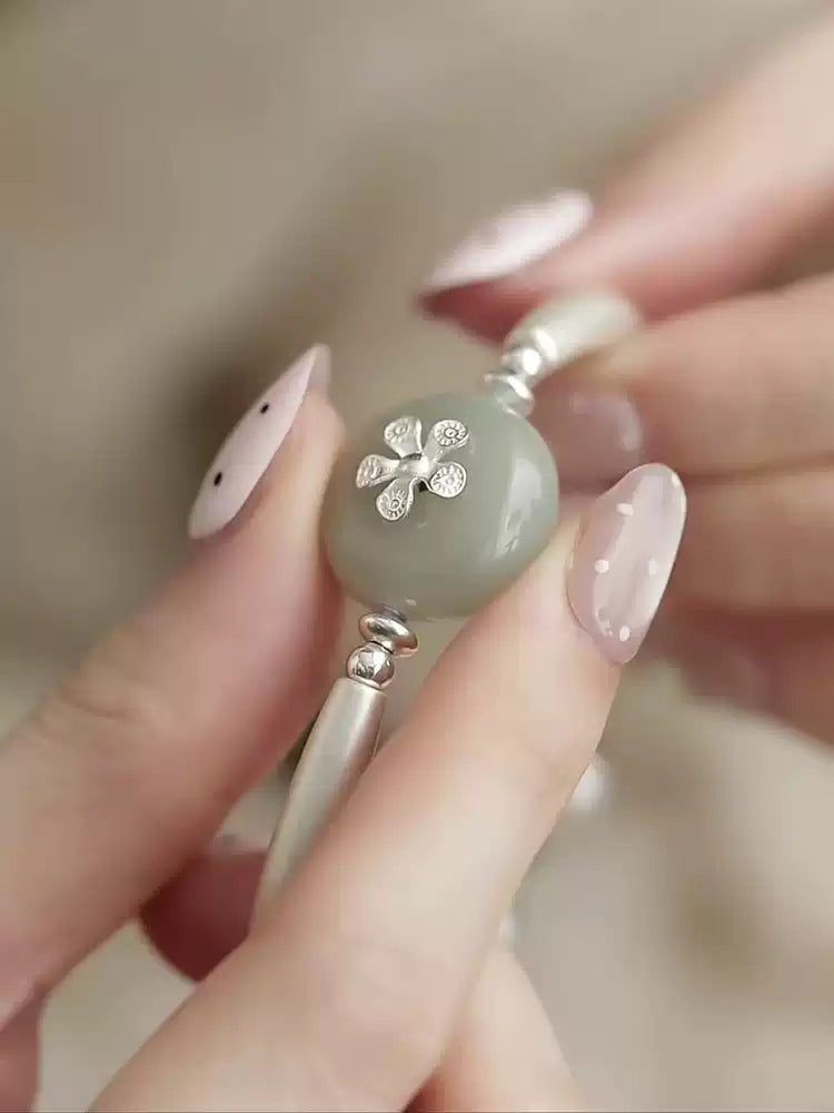 Close-up of pale green imitation jade-style bead and floral detail on the silver-tone bracelet