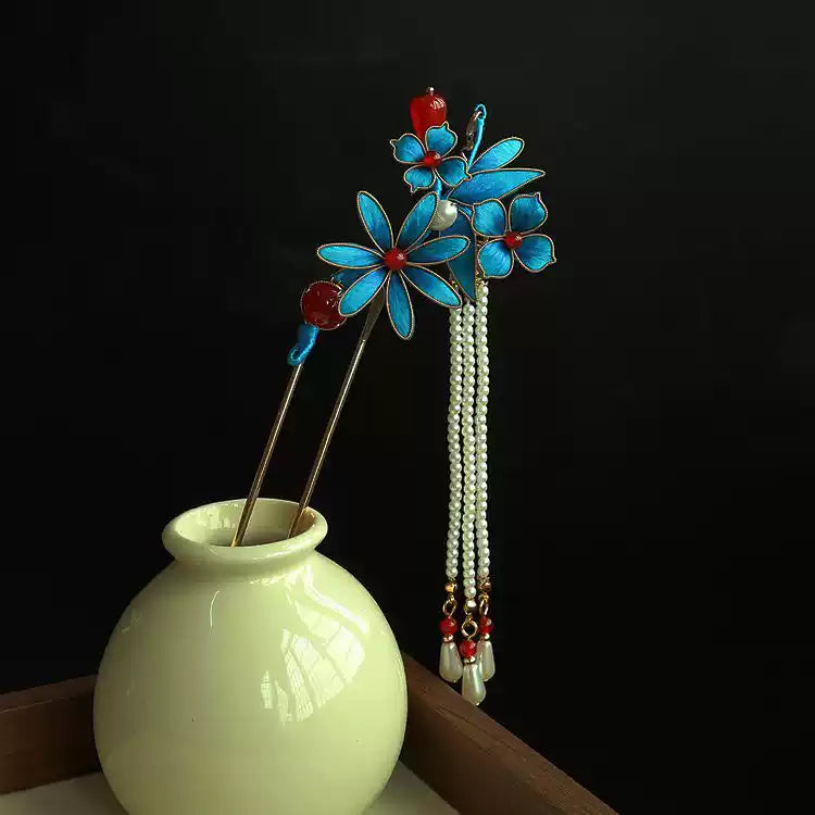 Blue floral hairpin pair styled in a vase with hanging bead strands; vase is a display prop