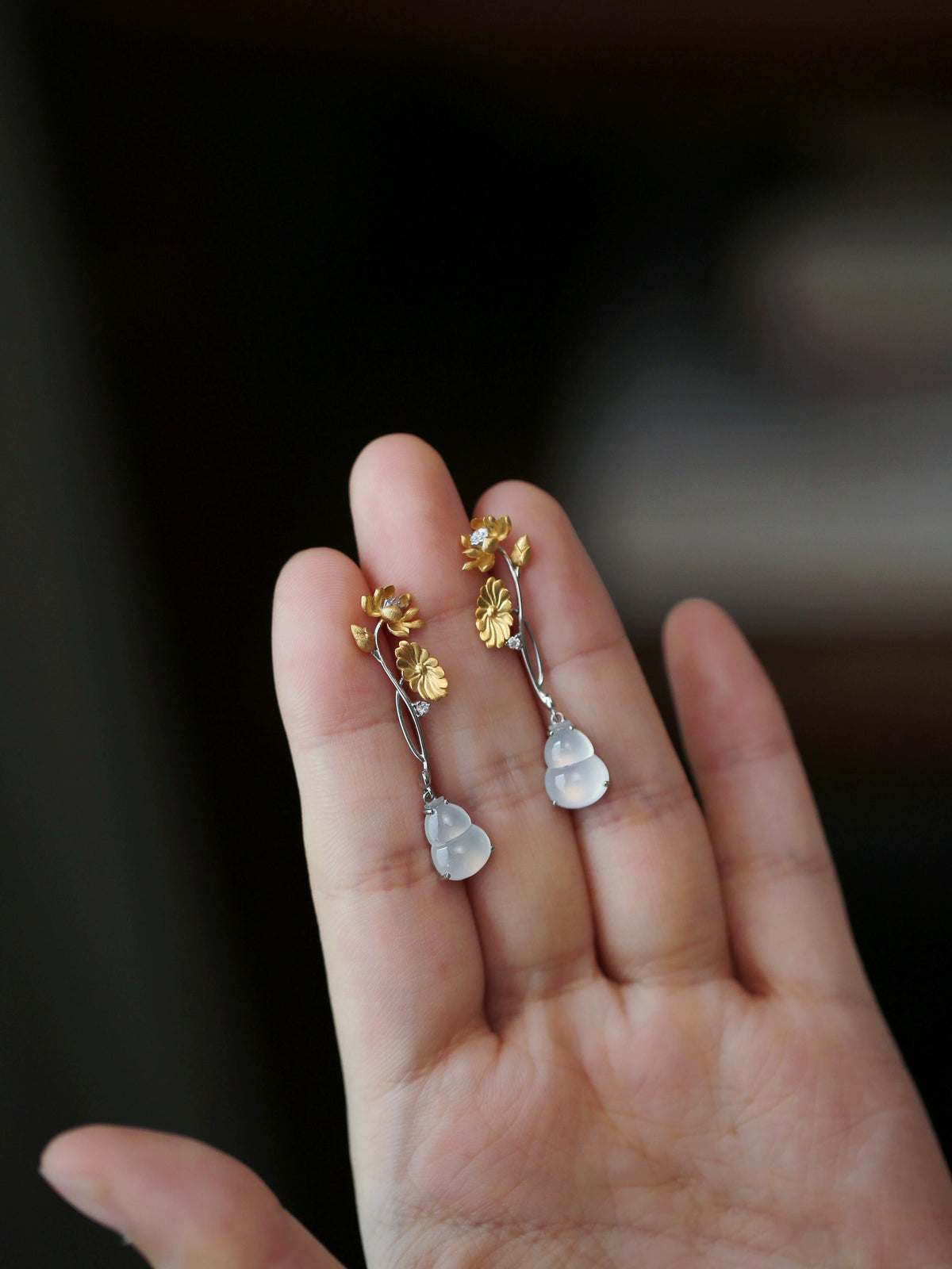 Close view of one floral earring with a pale imitation-jade-style gourd pendant.