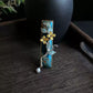 Close view of the floral branch and woven panel on a deep blue hair clip