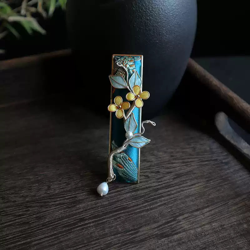 Close view of the floral branch and woven panel on a deep blue hair clip