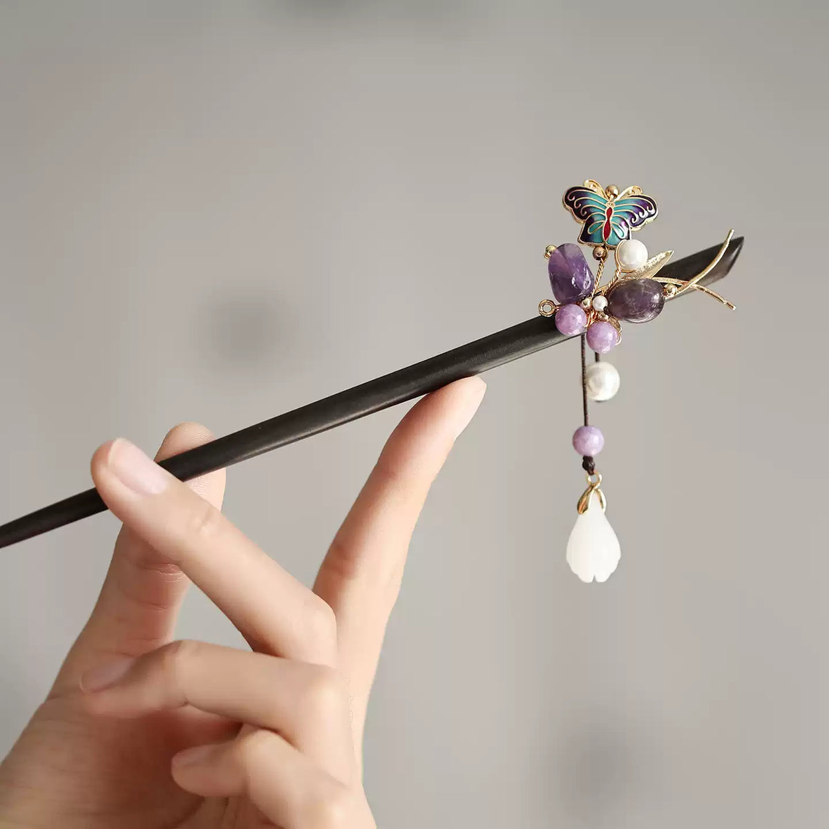Purple stone butterfly hair stick with dangling white bead accent, shown in hand