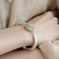 Silver-tone lotus pod cuff bracelet worn on the wrist, showing pale green bead and charm