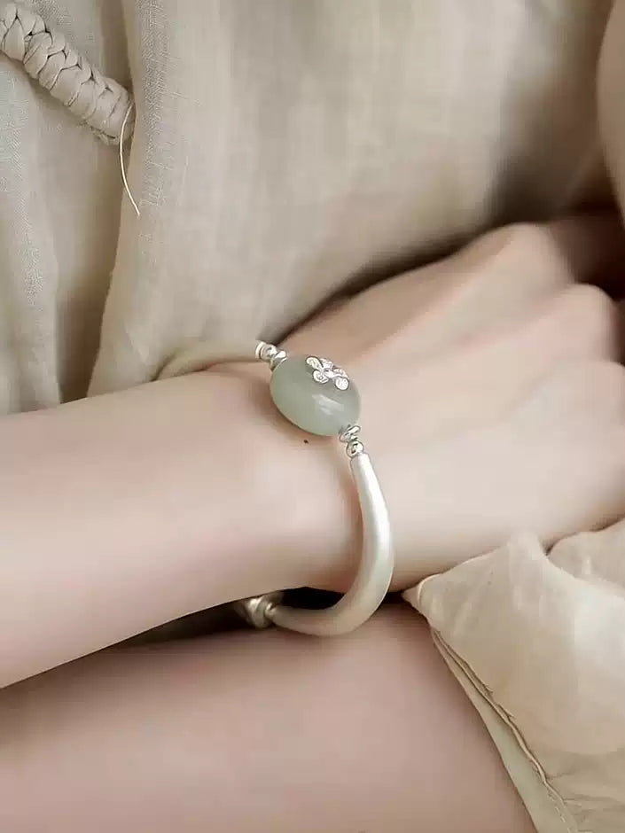 Silver-tone lotus pod cuff bracelet worn on the wrist, showing pale green bead and charm