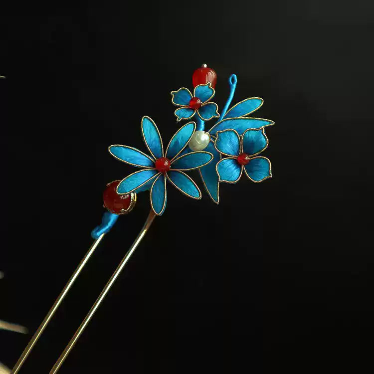 Close-up of blue floral details, red accents, and metal outlines on the hairpin pair