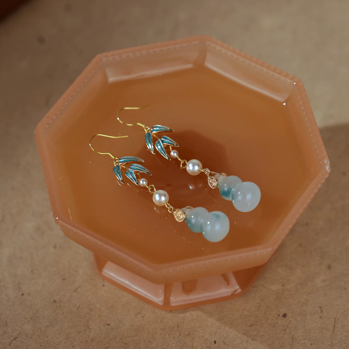 Blue-green gourd pendant earrings with imitation pearls on an amber-colored tray