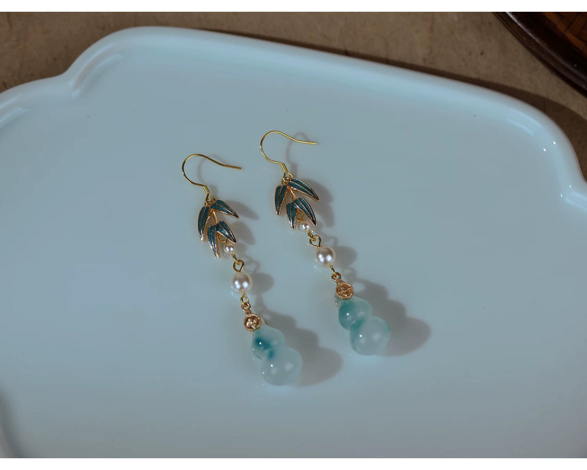 Bamboo leaf and gourd earrings with pierced-ear hooks resting on a white dish