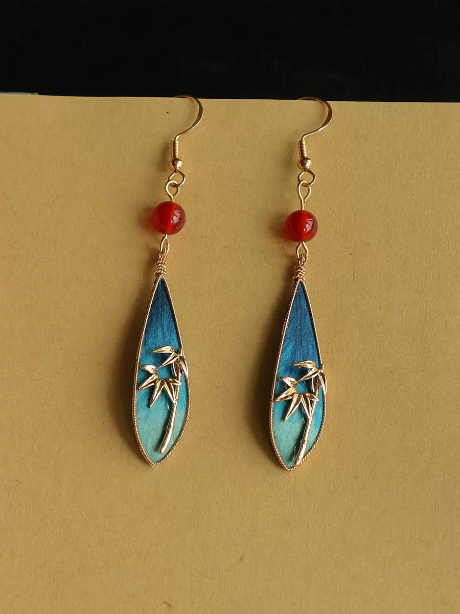 Front view of the blue-green bamboo motif earrings with red bead accents