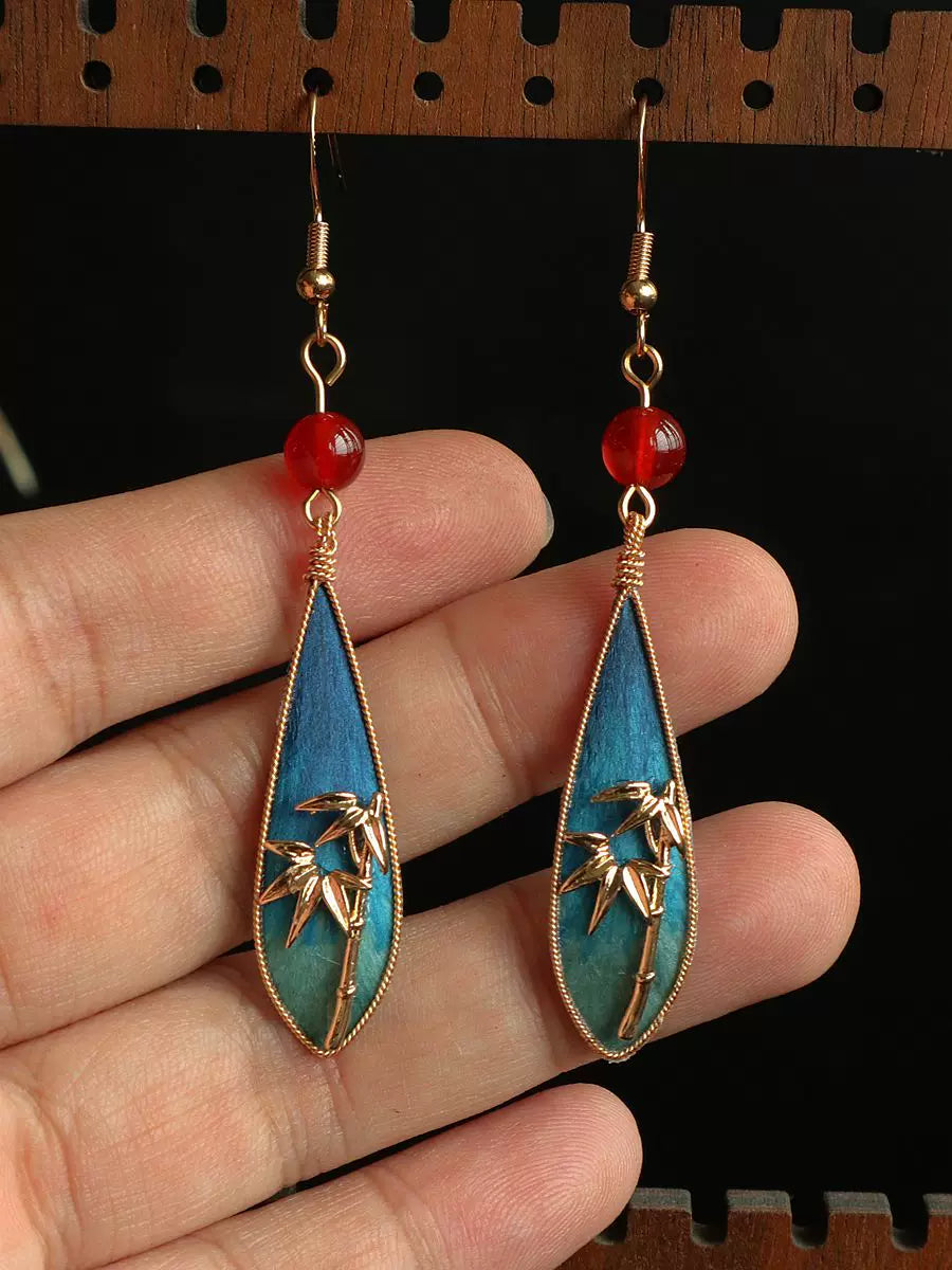 Hand-held scale view of the bamboo leaf earrings showing their drop shape