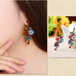 Two views of blue cloisonne earrings worn and displayed beside a teapot