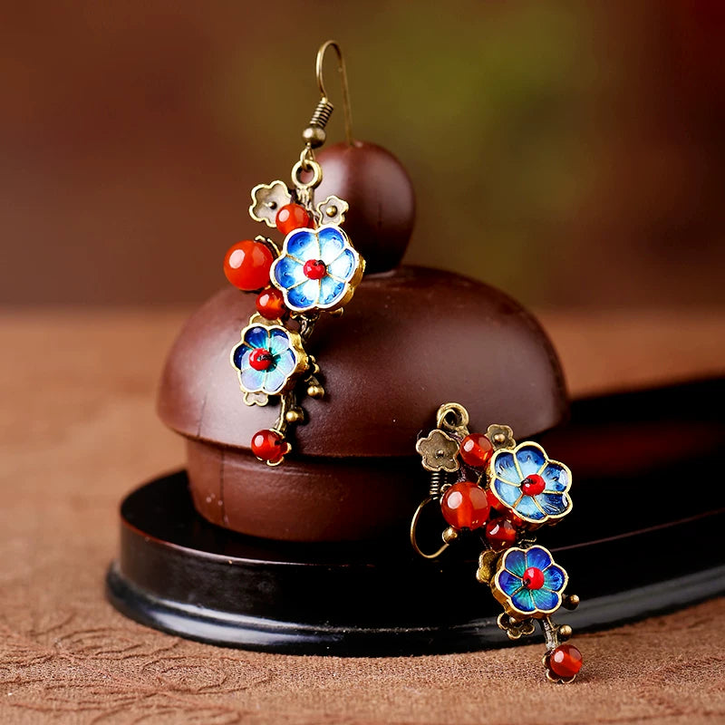 Pair of floral cloisonne and red agate earrings displayed on a small teapot