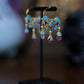 Single blue enamel floral tassel earring shown on a display stand.