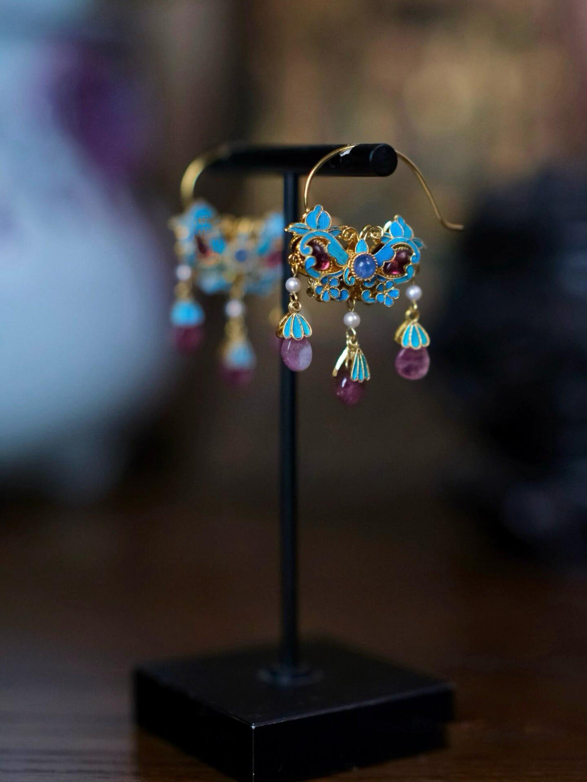 Single blue enamel floral tassel earring shown on a display stand.