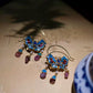 Close-up of blue enamel flower earrings with gold-tone filigree details and dangling purple accents.