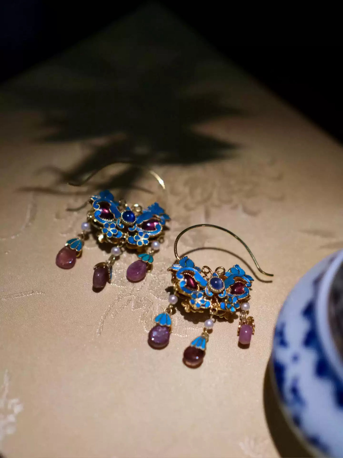 Close-up of blue enamel flower earrings with gold-tone filigree details and dangling purple accents.