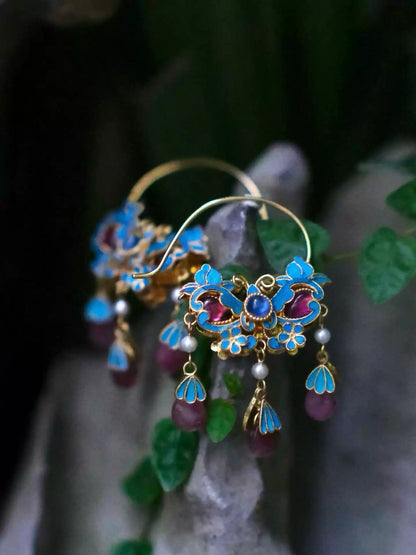 Pair of blue enamel flower drop earrings with purple accents and tassels on a light background.
