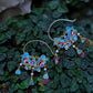 Pair of blue enamel floral tassel earrings displayed against green leaves.