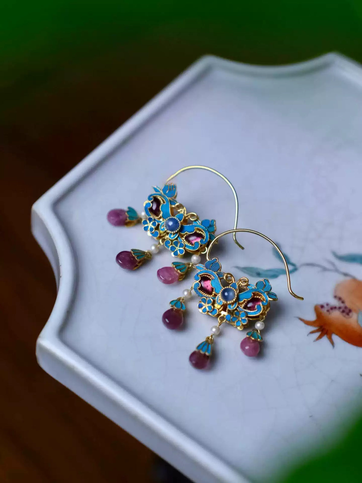Pair of blue enamel flower drop earrings arranged in a white jewelry tray.