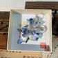 Overhead view of handmade blue iris hair accessory in box