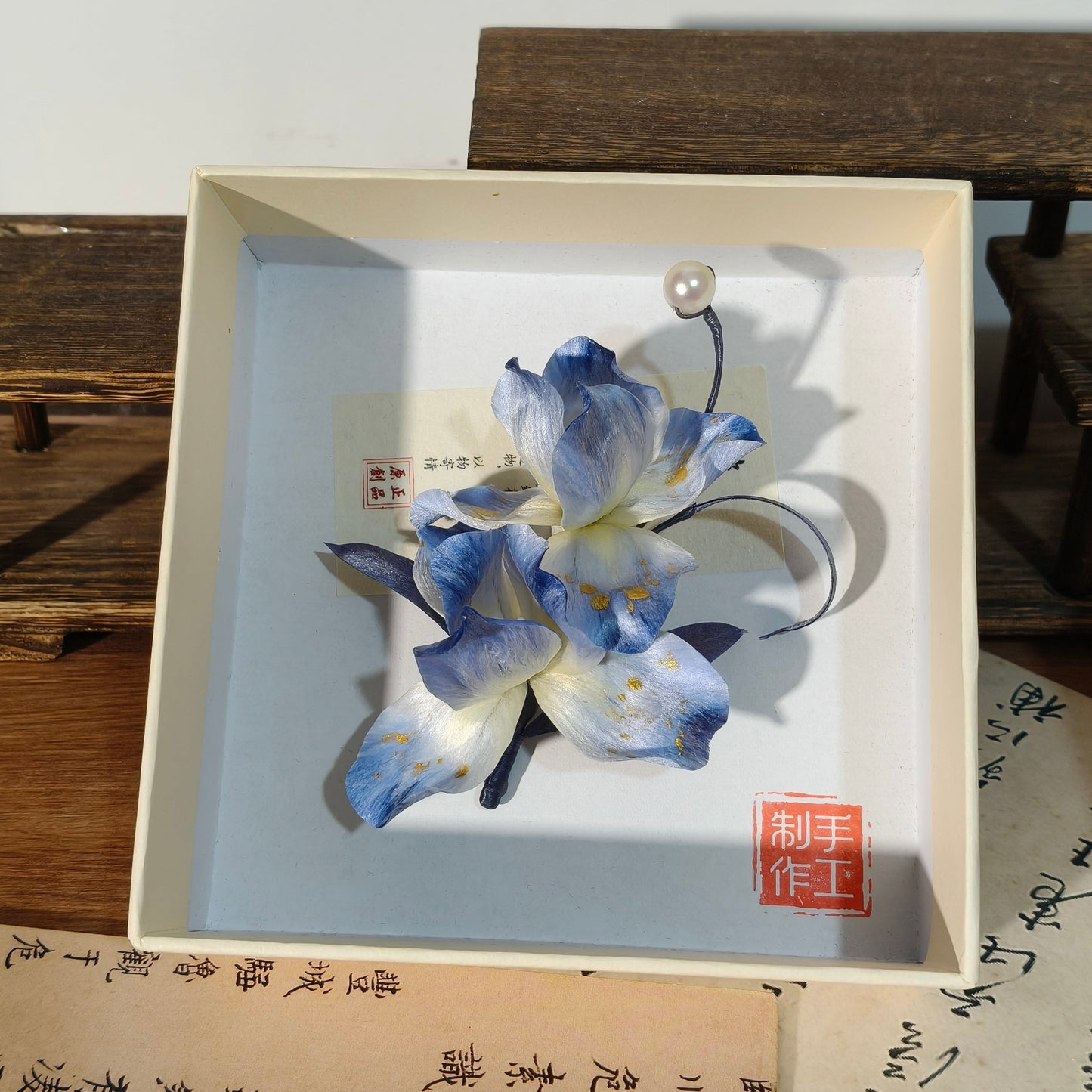 Overhead view of handmade blue iris hair accessory in box