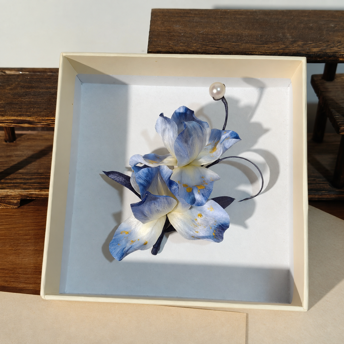 Blue and ivory iris brooch with gold accents and a pearl detail in a presentation box