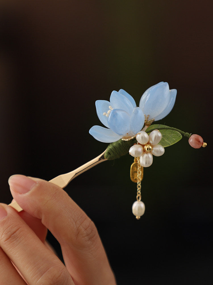 Detail view of the blue magnolia flower, green leaf, and dangling accents