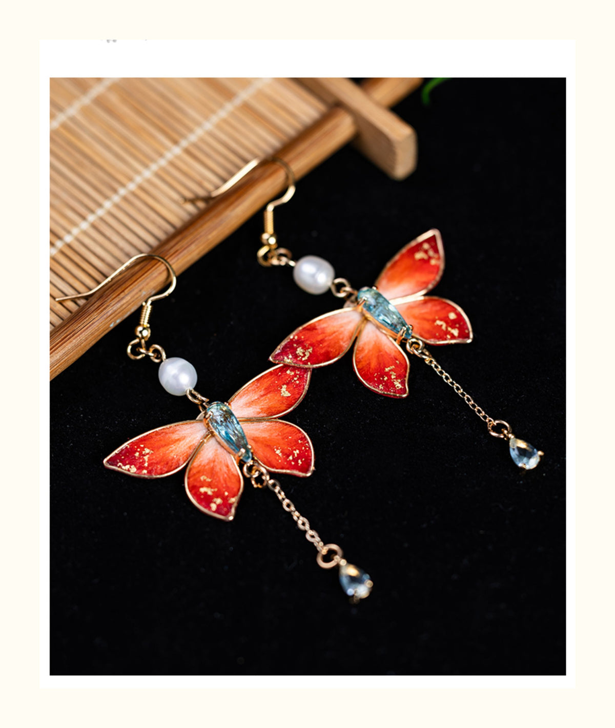 Close view of red butterfly earrings with pearl and chain-drop details