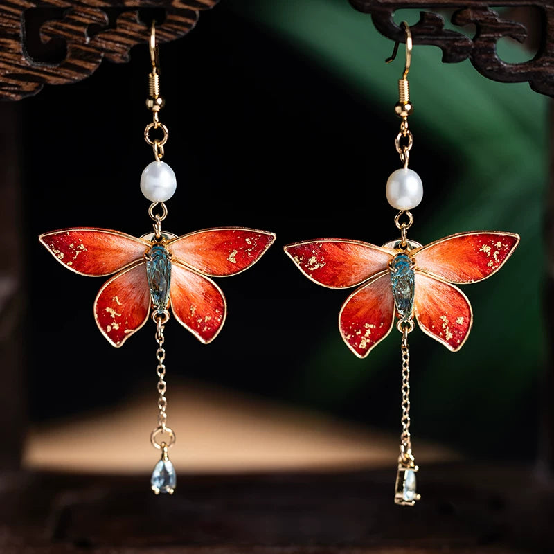 Pair of red butterfly drop earrings with pearl accents, chain dangles, and ear hooks